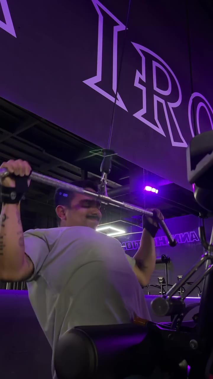A wrist strap on a lat pulldown bar under purple gym light